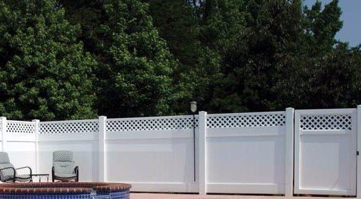 White vinyl fence with lattice detail surrounds a pool area with trees in the background.