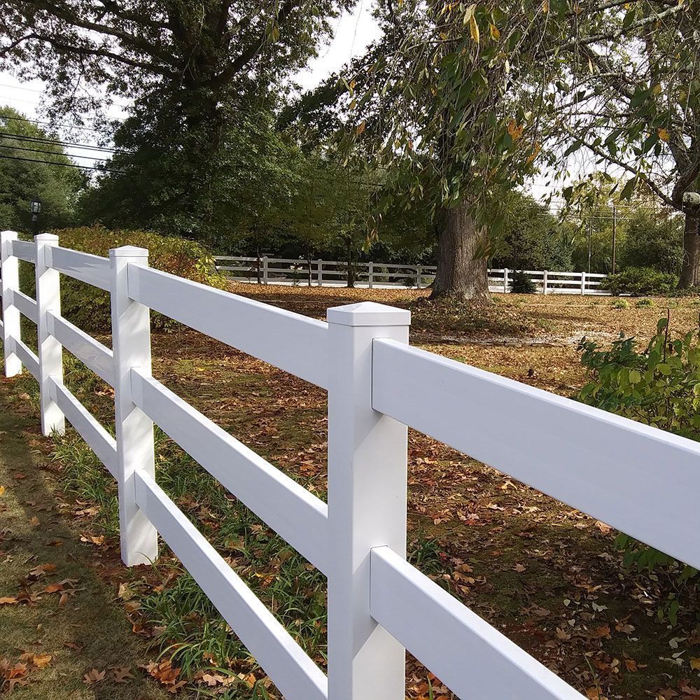 White three-rail fence in a grassy area with trees in the background.
