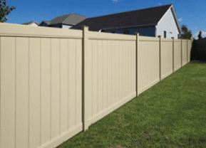 Tan vinyl fence in a backyard with green grass and a house in the background.