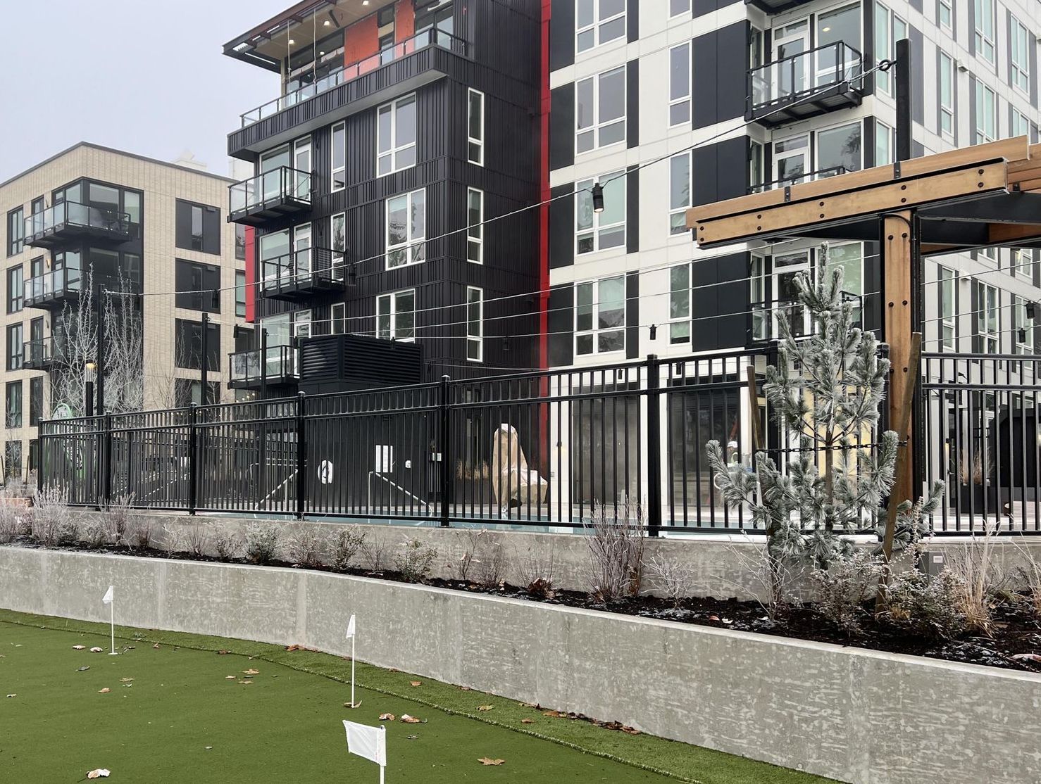 Modern apartment buildings behind a black fence, overlooking a small putting green.
