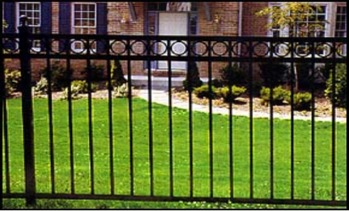 Black metal fence in front of a green lawn and a house with a white door.