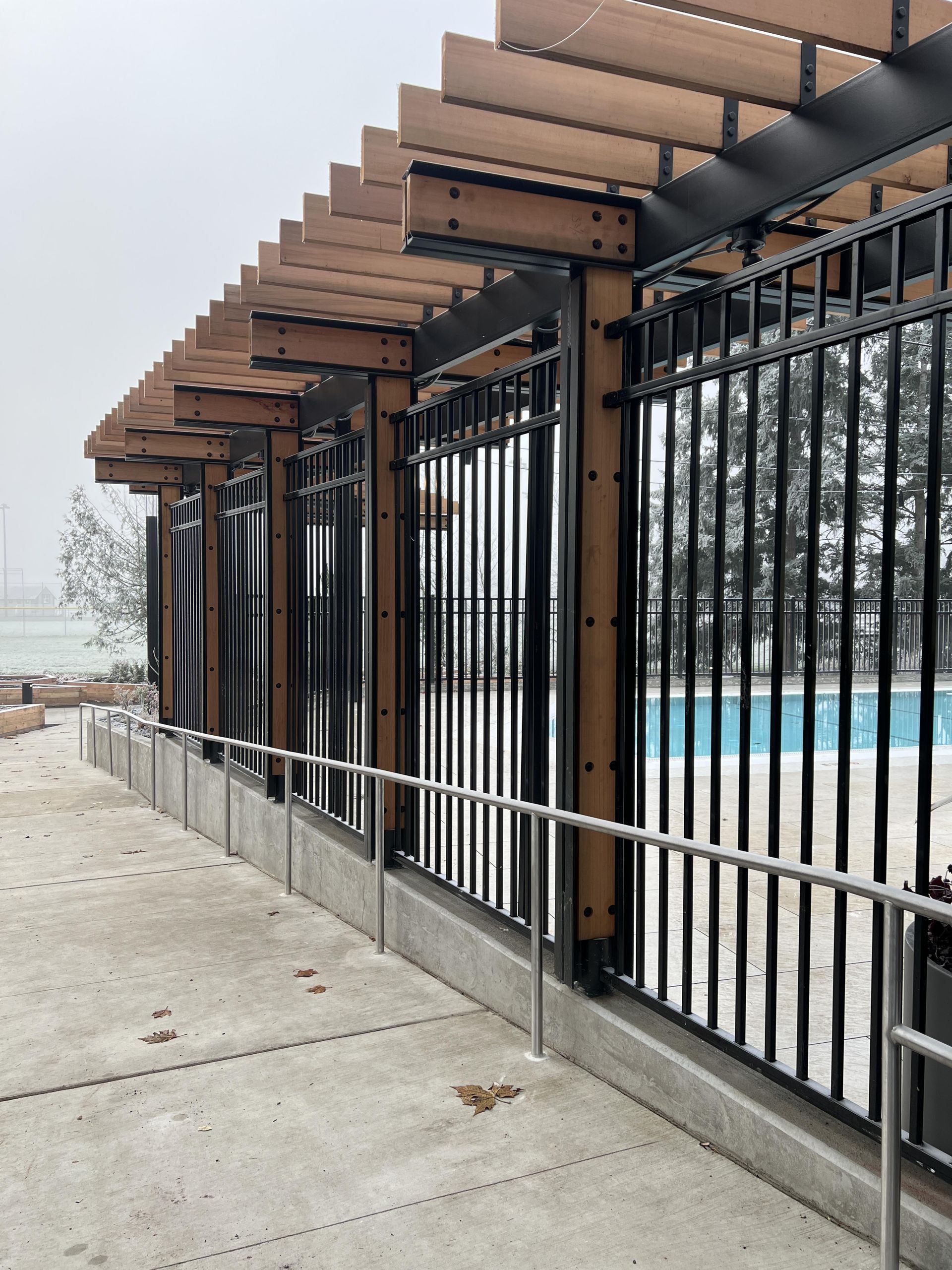 A black metal fence with brown beams and a walkway next to a pool.