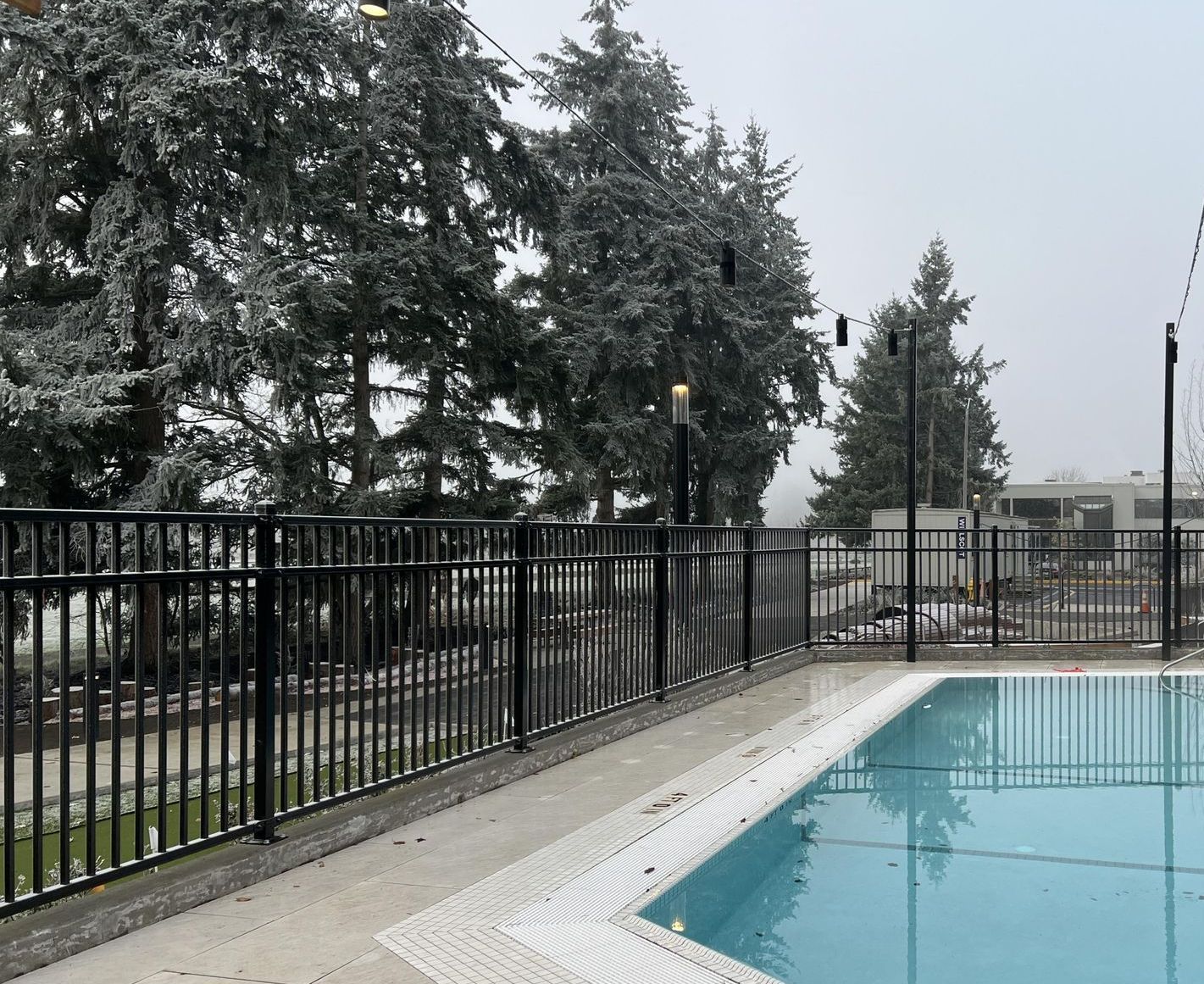 Poolside scene with black fence, string lights, and trees dusted with snow.