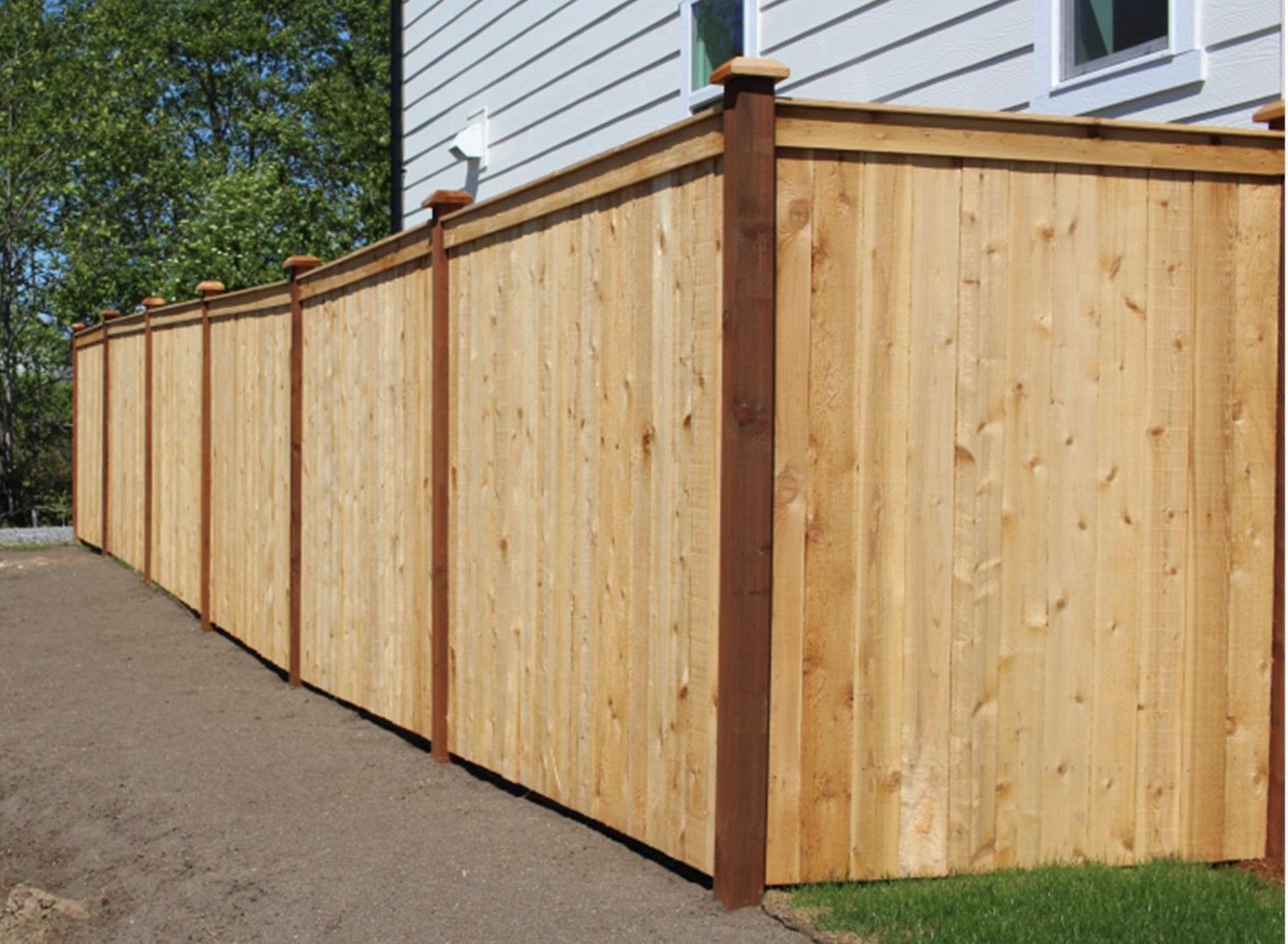Wooden privacy fence with dark brown posts and light wood panels, bordering a yard next to a house.