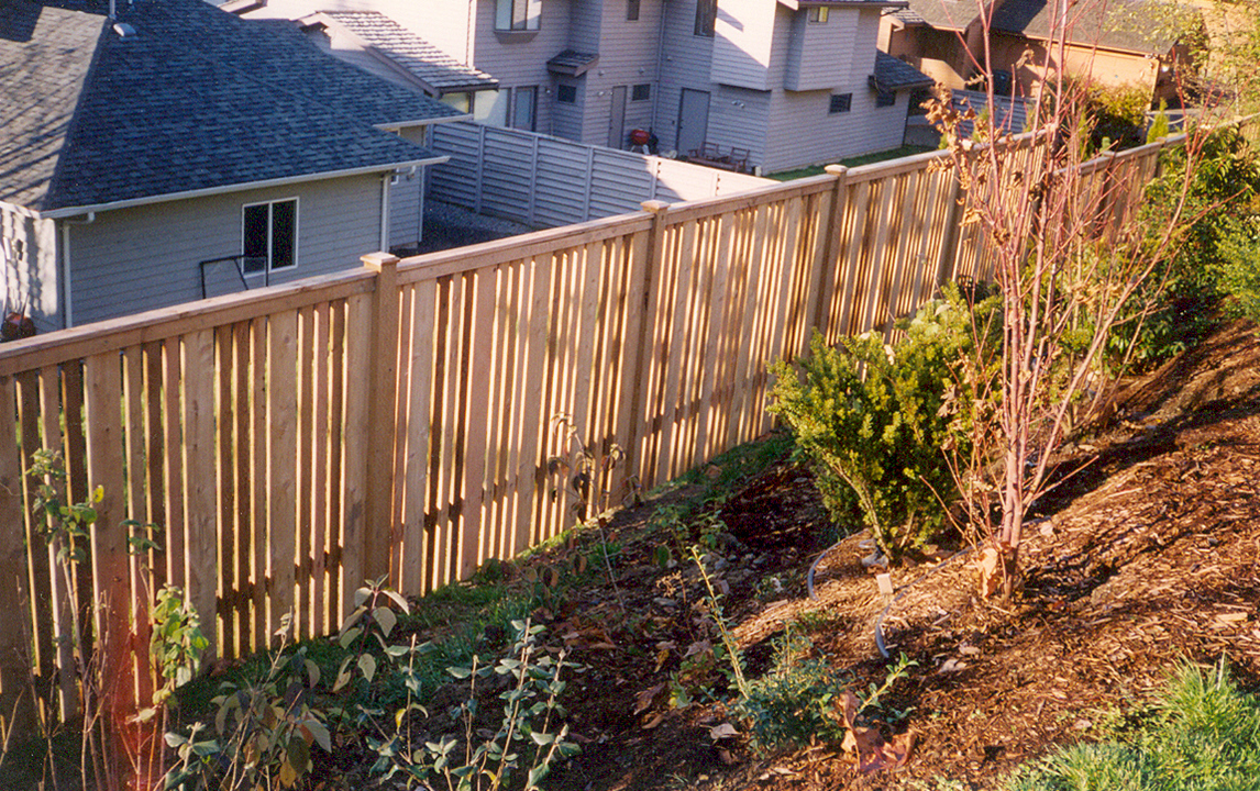 Wooden fence on a hillside, separating a yard from a house.
