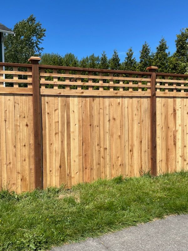 Wooden fence with lattice top, brown posts, and green grass against a blue sky.