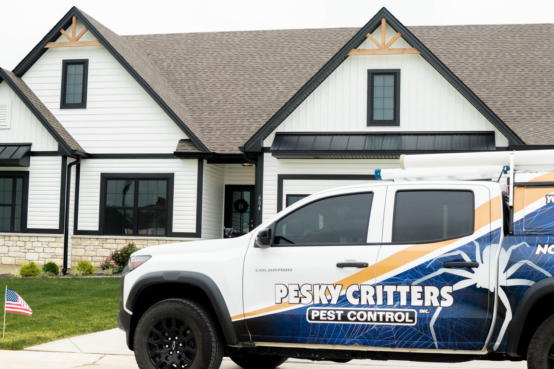 A white Pesky Critters Pest Control truck parked in front of a modern white house with black trim and a gabled roof.