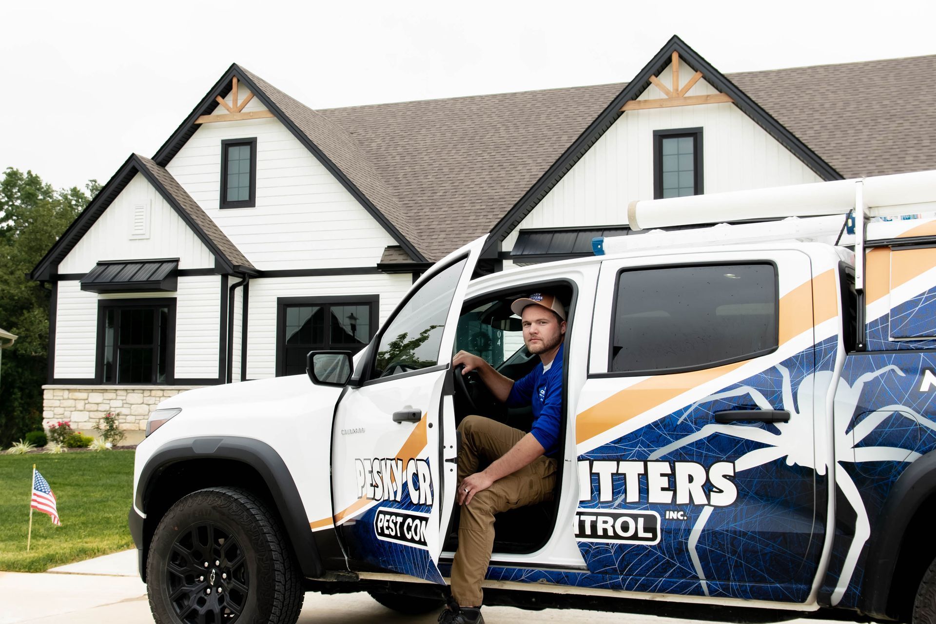 A pest control worker exits a branded truck parked in front of a modern white house.