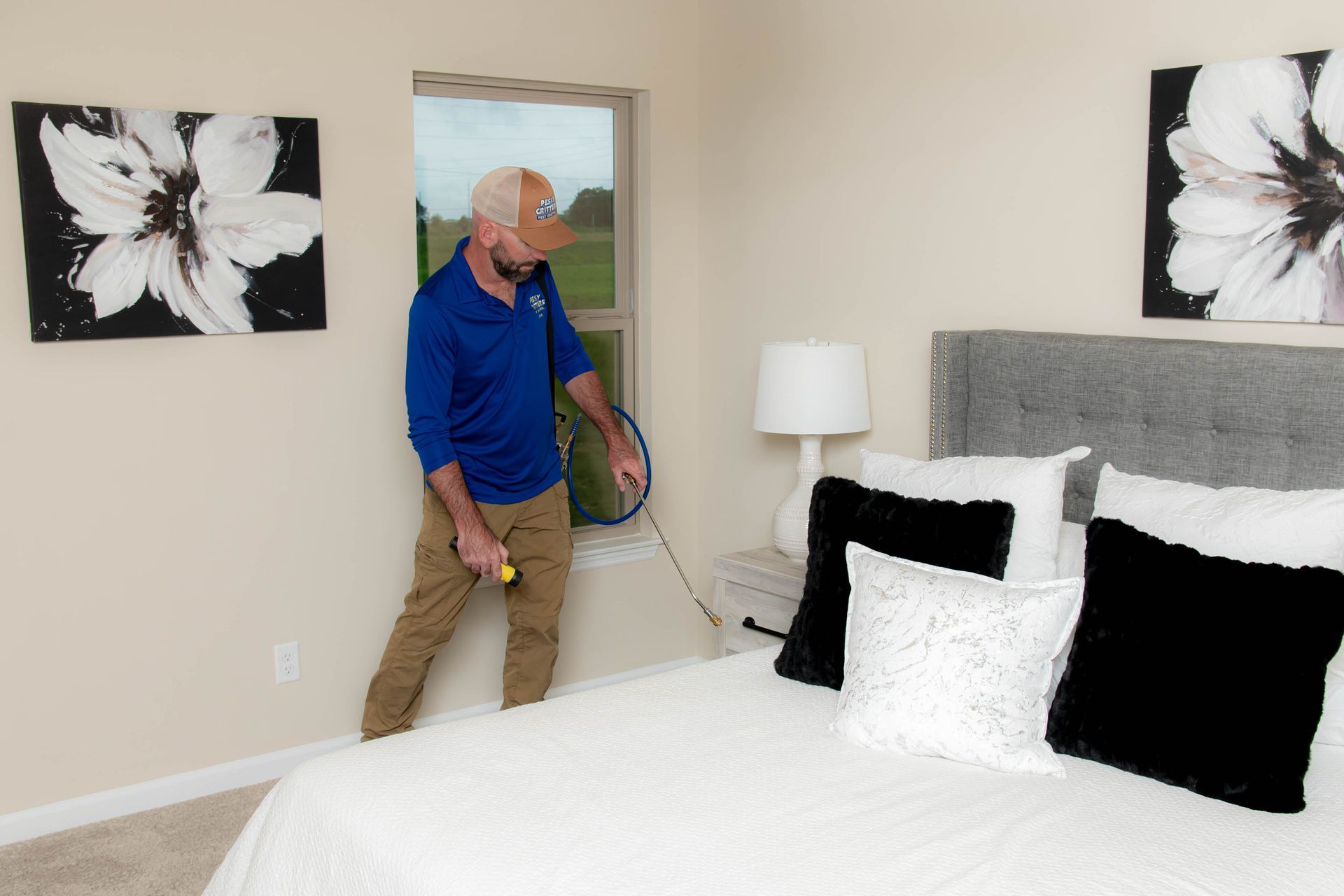 A person in a blue shirt inspects a bedroom with a handheld device near a bed with a gray headboard and decorative pillows.