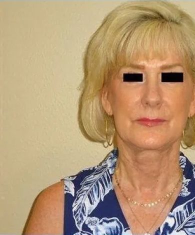 Woman with blonde hair, wearing a blue floral top and gold jewelry, looking at the camera.