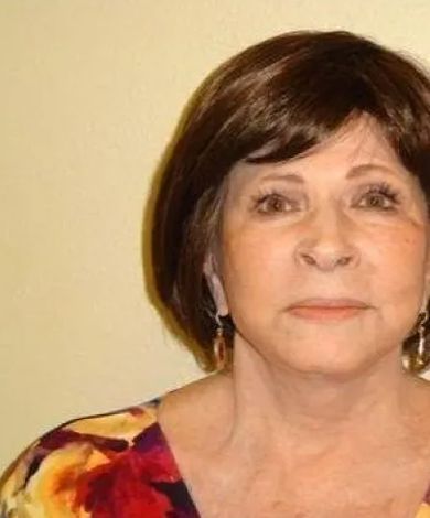 Woman with short brown hair and a colorful top against a pale background.