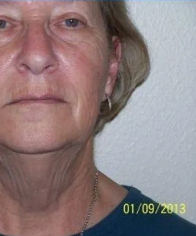 Woman, slight smile, wrinkles, pale skin, wearing a silver chain, close-up. Light background.