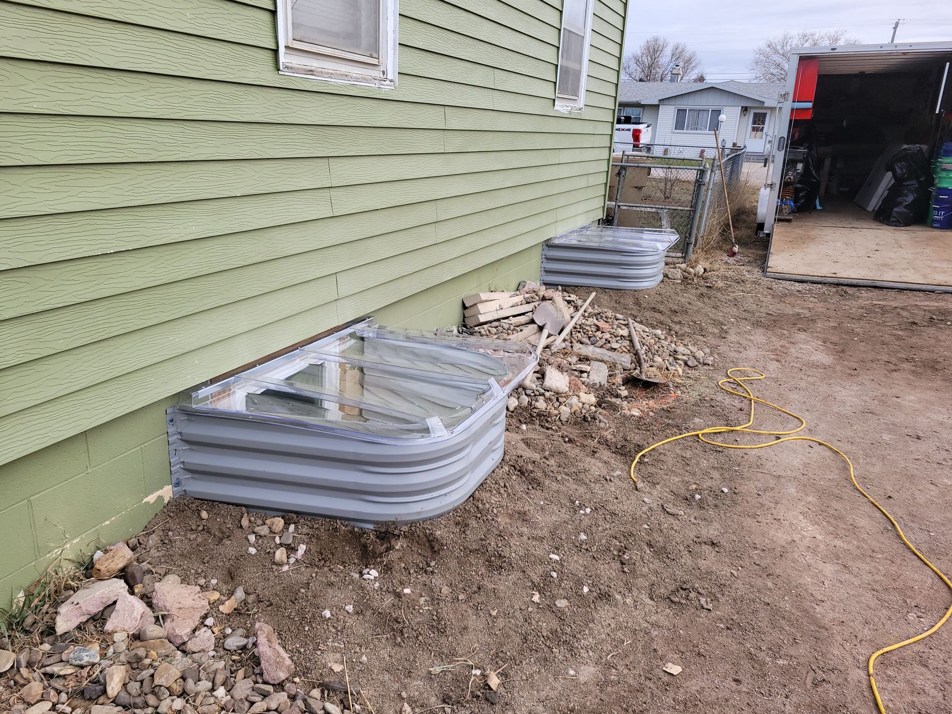 Green house exterior with corrugated window wells in dirt.