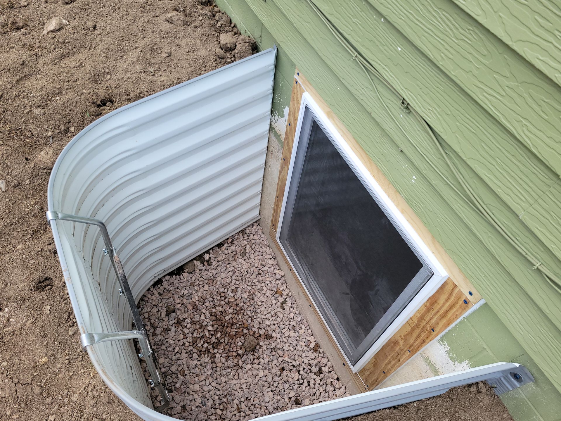 Metal window well, gravel, and window in a building's foundation.