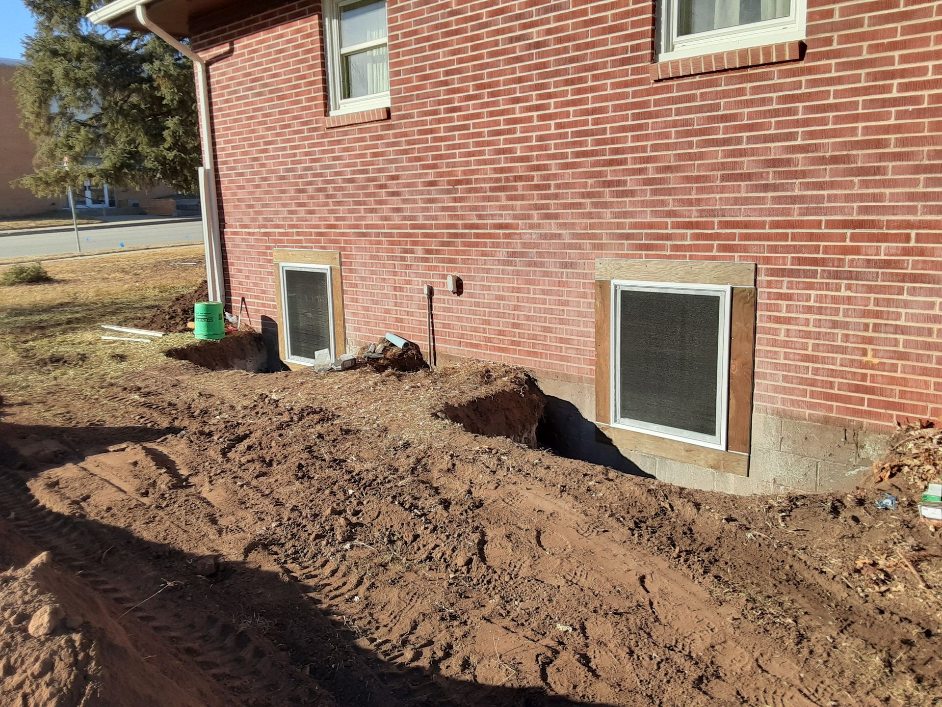 Exterior of brick building with excavated earth around basement windows.