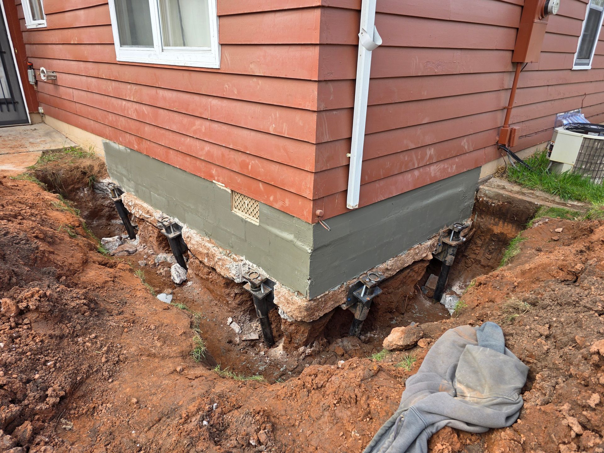 House foundation repair: metal support jacks hold up a building corner, dug into surrounding dirt.