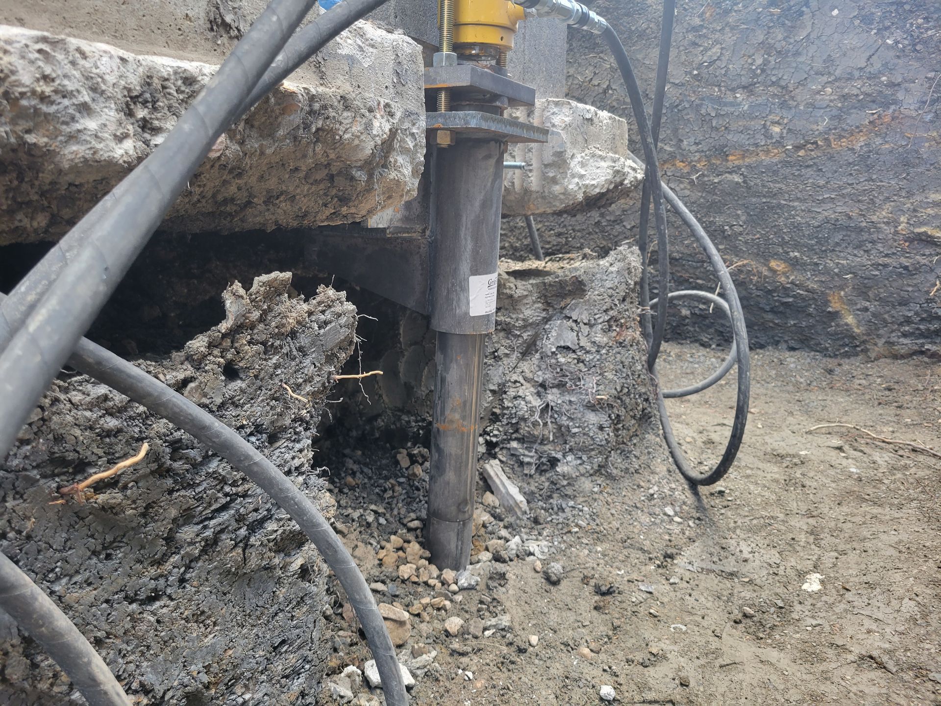 Jackhammer breaking up concrete in a construction setting. Black hoses and grey rock.