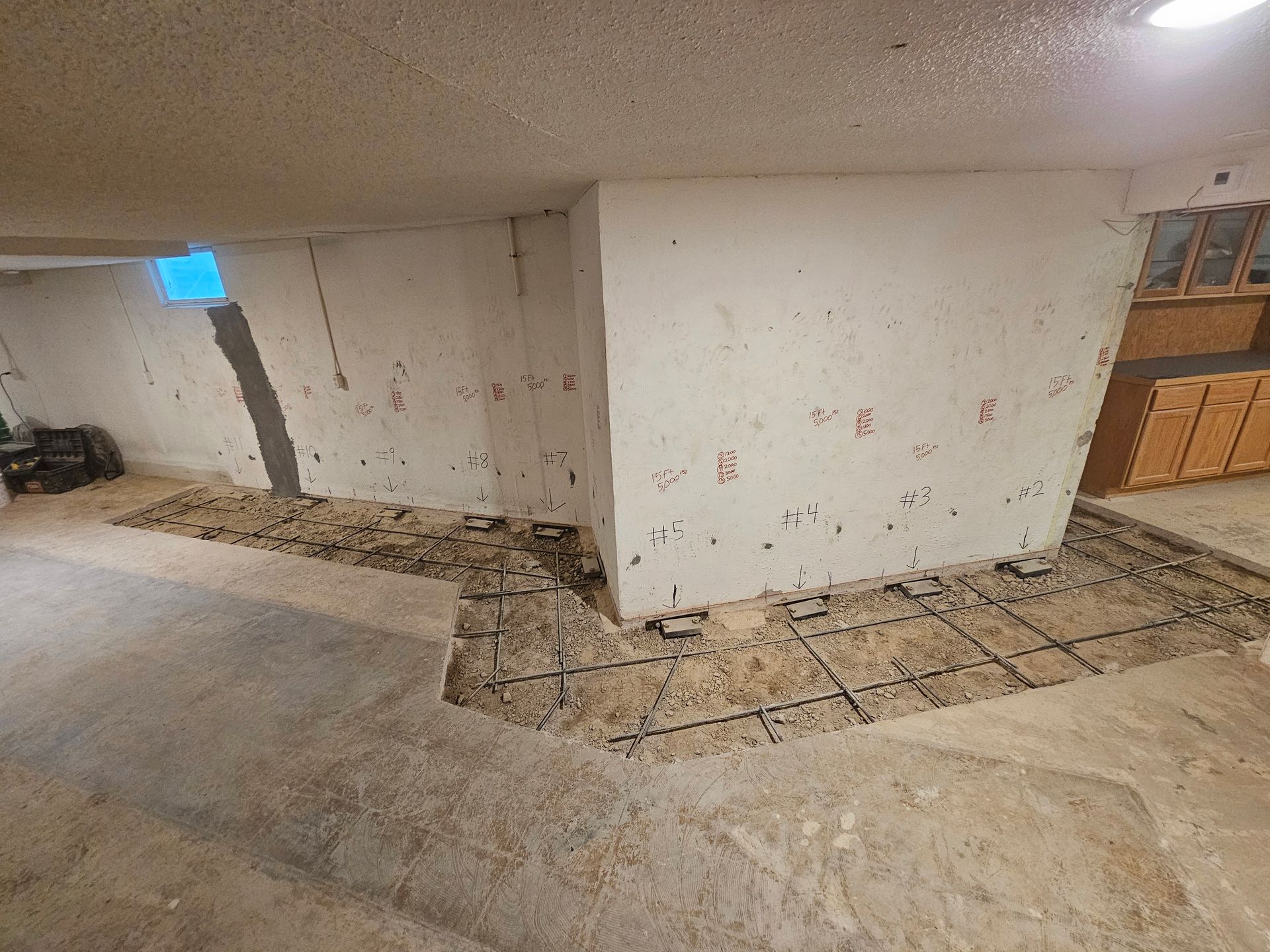 Basement renovation in progress, concrete floor with exposed rebar, unfinished walls, cabinet visible.