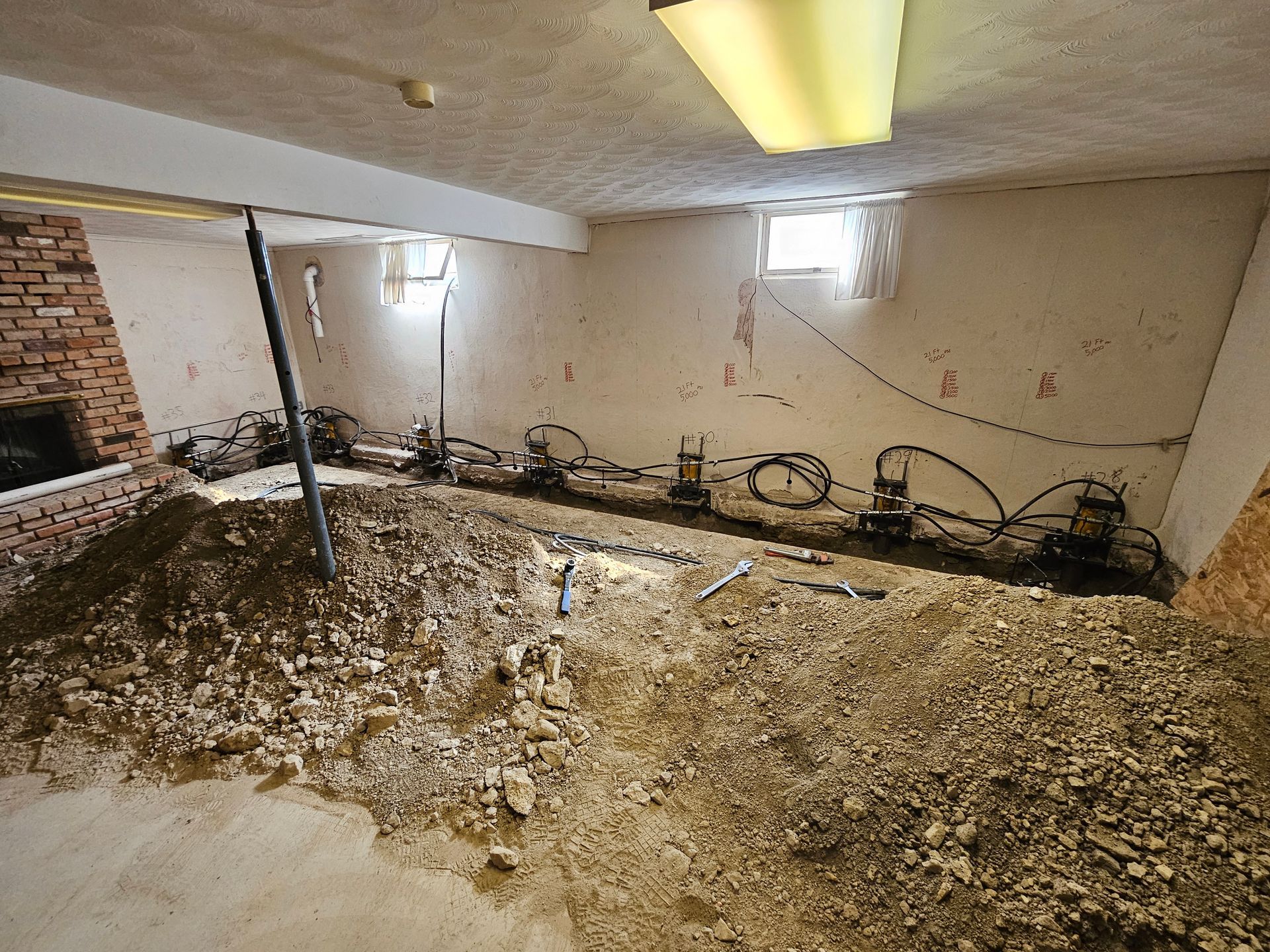 Basement renovation with dirt pile, support jacks along wall, fireplace, and exposed wiring.