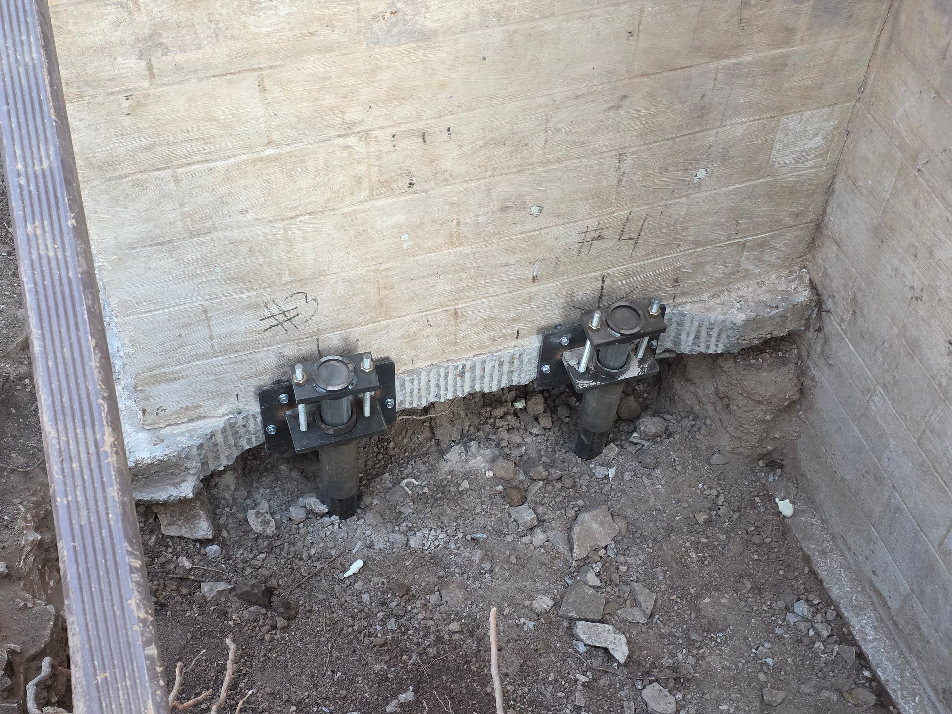 Two helical piers installed to support a concrete foundation, visible in a dug-out area.