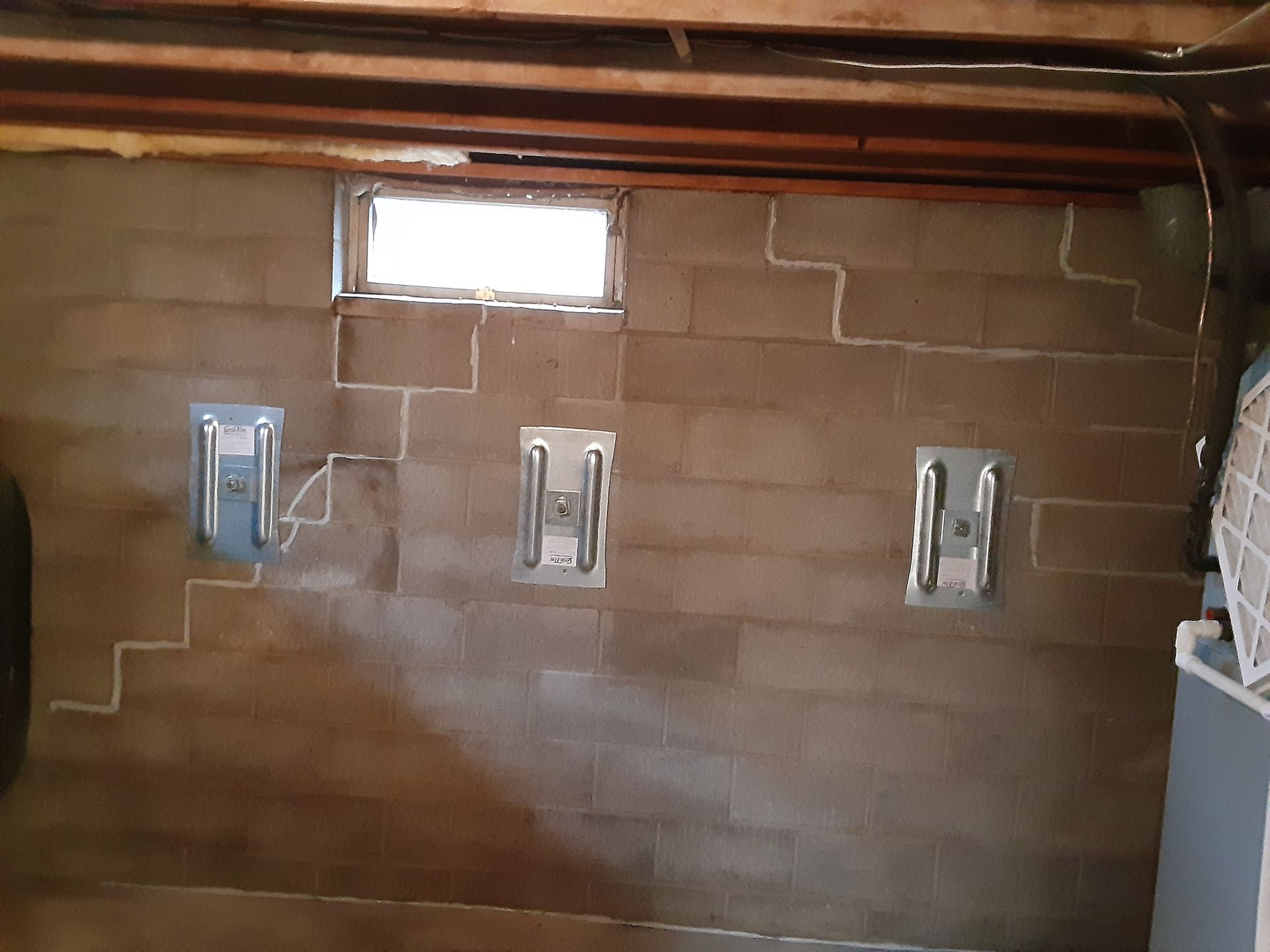 Basement wall with three wall anchor plates, small window, and visible cracks on the block.