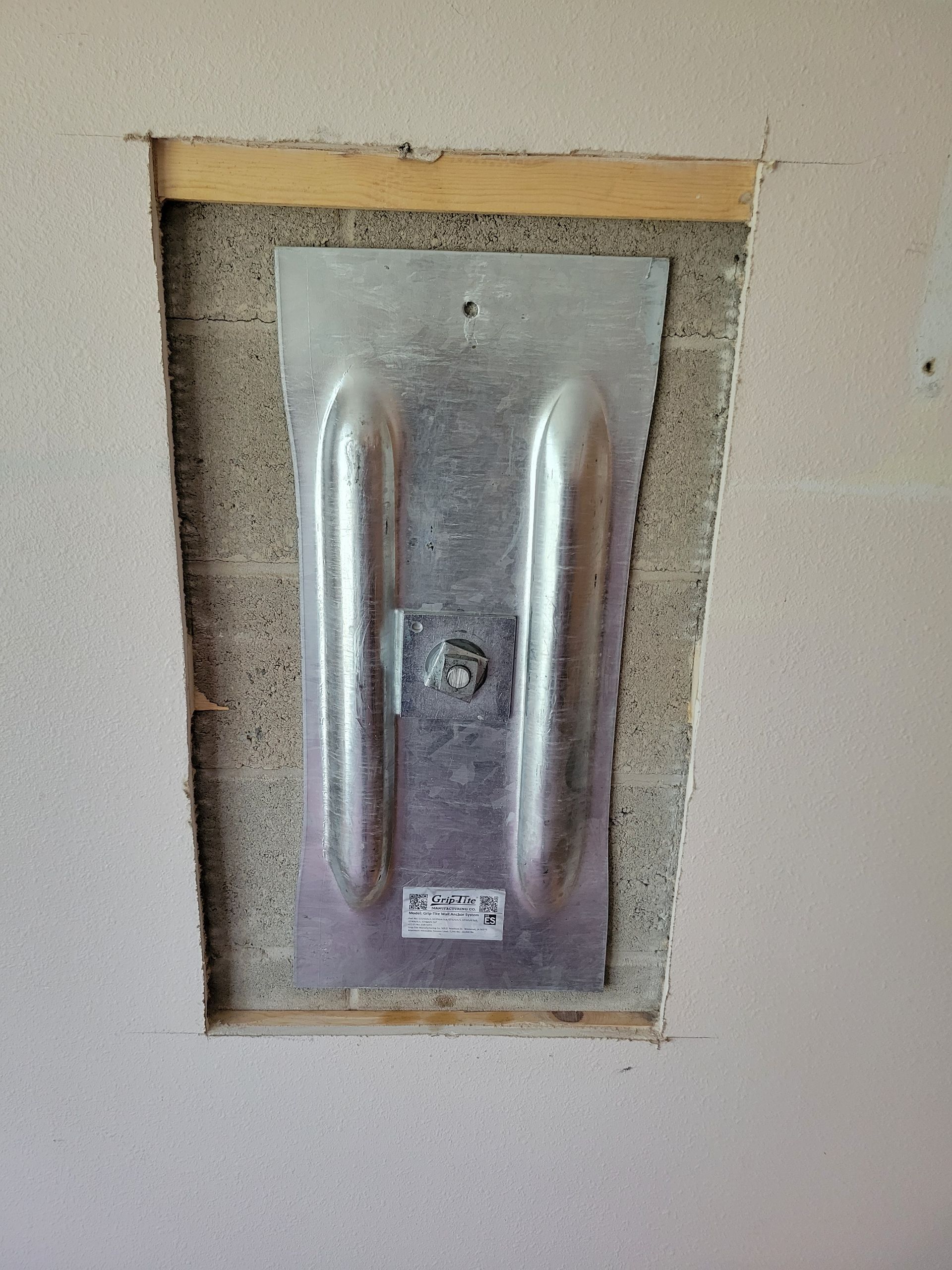 Metal mounting plate installed in a wall opening, fastened with a bolt.