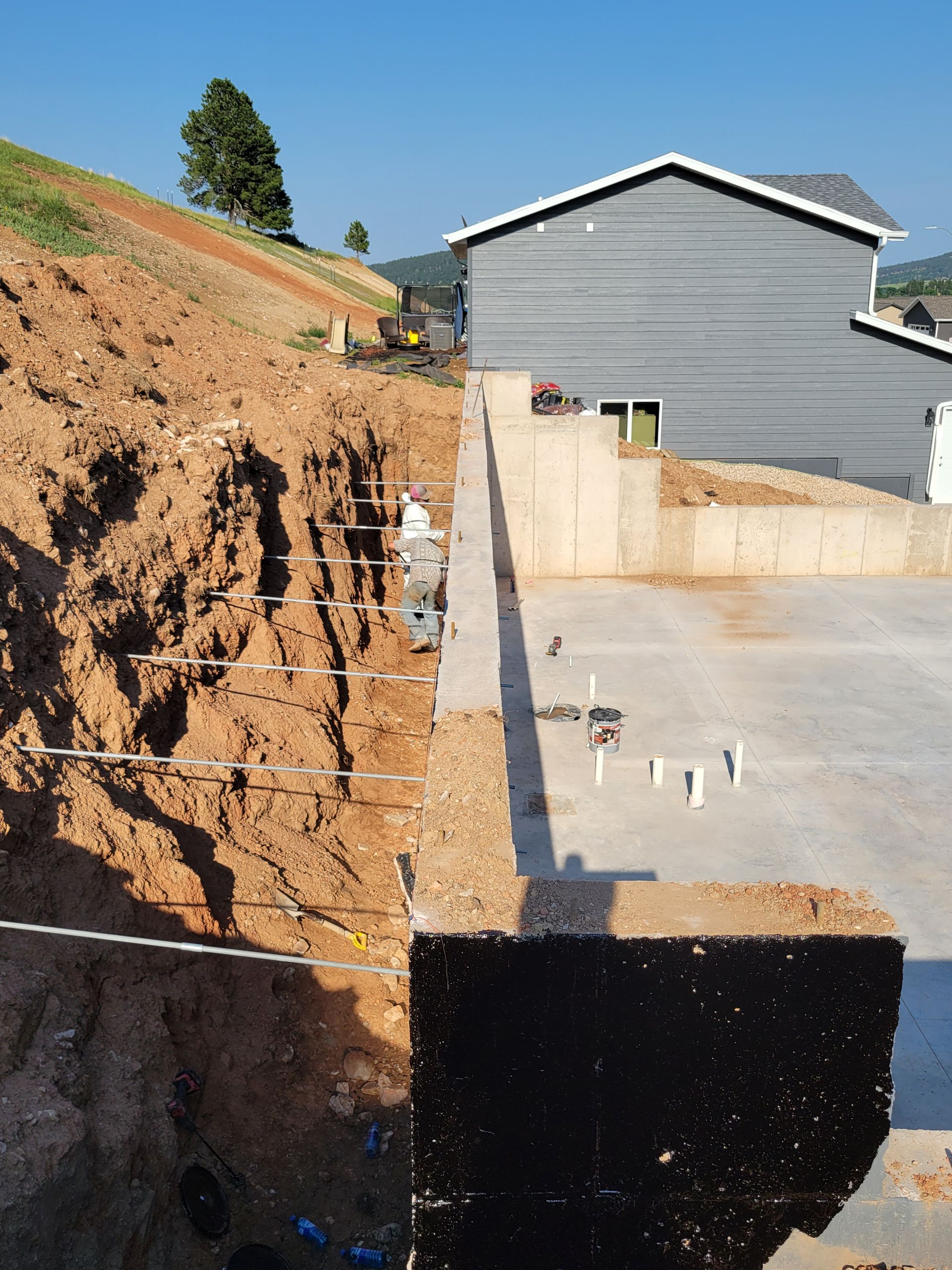 Construction site with a concrete foundation next to an excavated hillside.