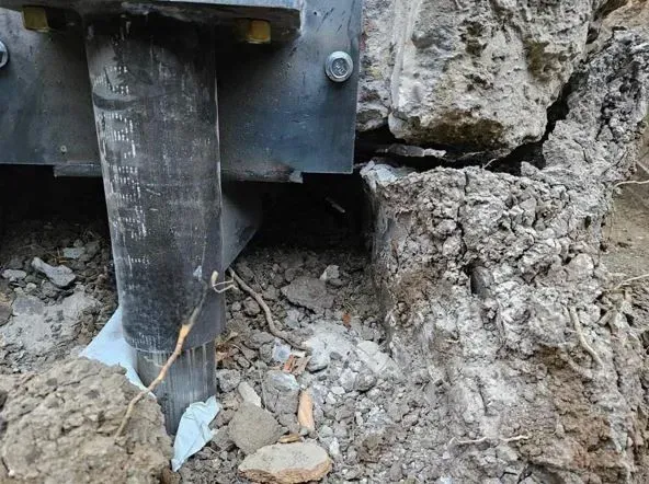 Metal post embedded in soil, adjacent to a broken concrete foundation.