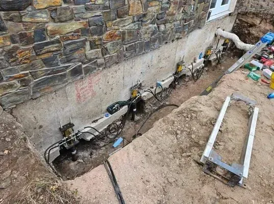 Foundation repair project: metal support brackets bolted to a concrete foundation. Soil trench is visible.