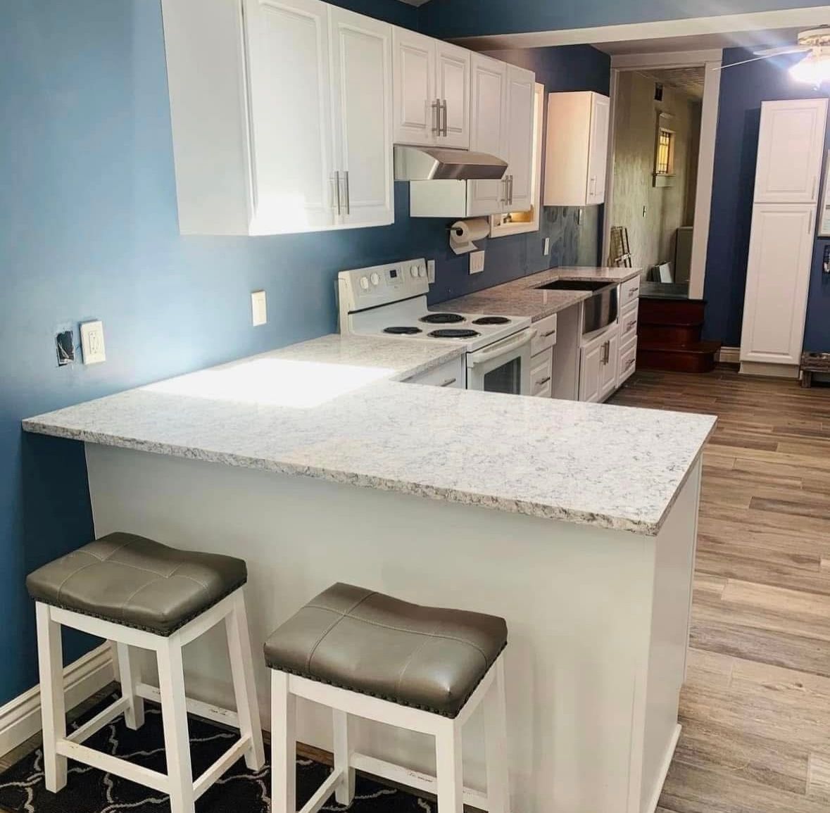 Bright kitchen with white cabinets, blue walls, granite island, and two stools.