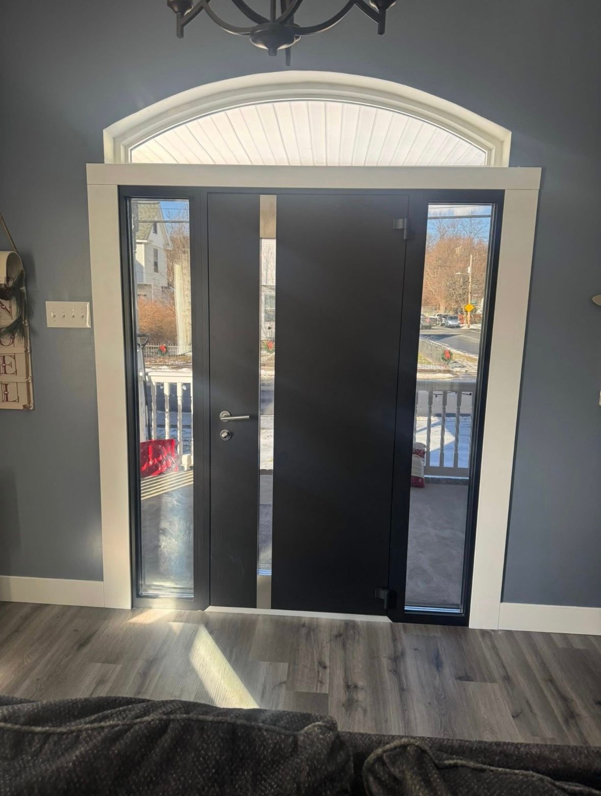 Black front door with narrow glass sidelights and arched transom in a gray entryway.