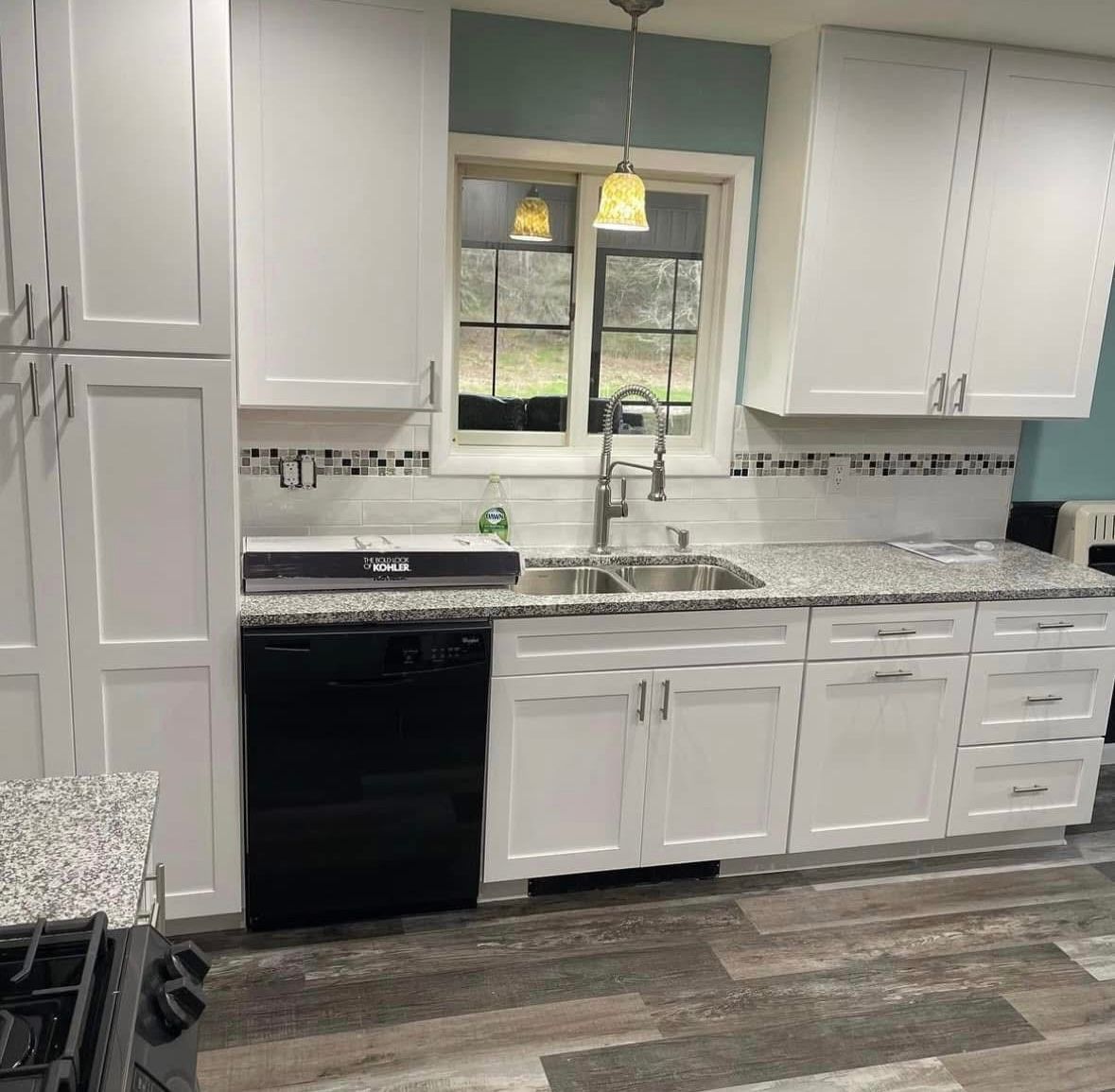 Bright white kitchen with black appliances, granite counters, and a window above the sink.