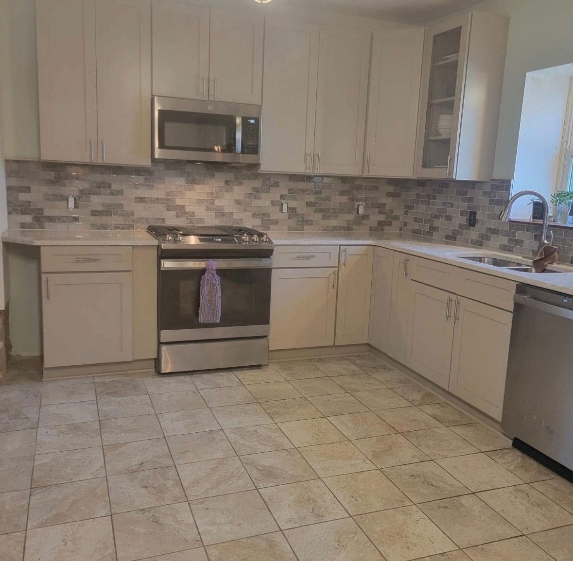 Bright kitchen with white cabinets, stainless steel appliances, tiled backsplash, and beige tiled floor