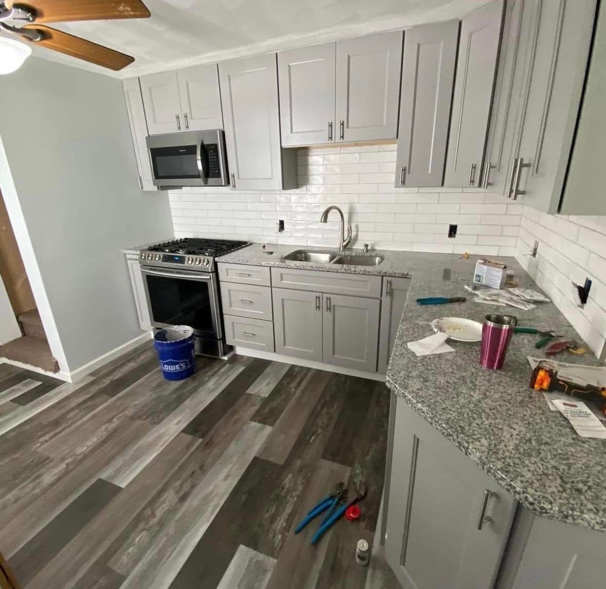 Modern kitchen with gray cabinets, stainless appliances, granite counters, and tools on the floor.