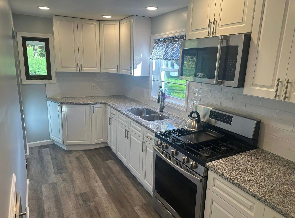Bright kitchen with white cabinets, granite counters, stainless stove, and wood-look flooring