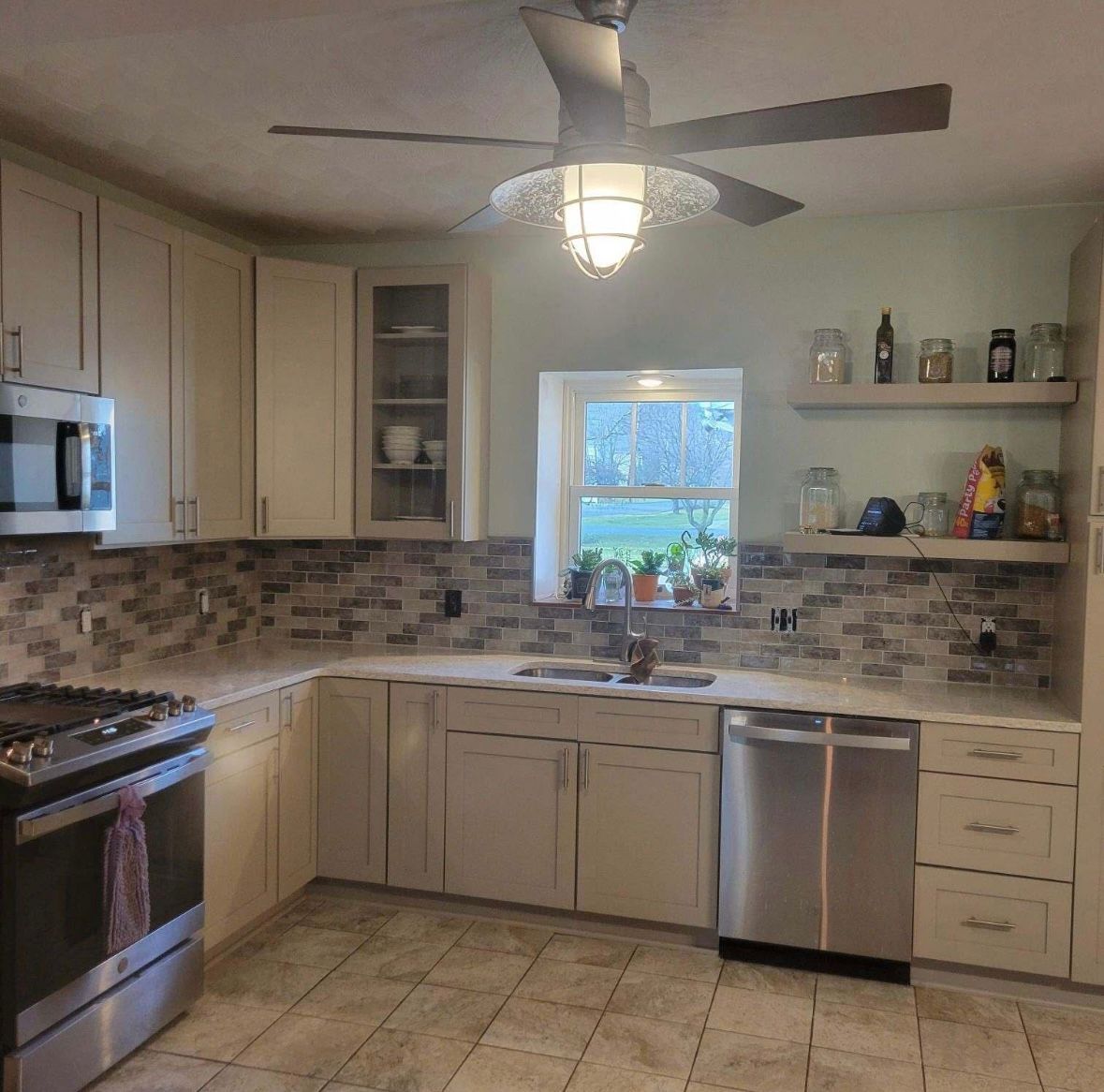 Bright modern kitchen with white cabinets, mosaic backsplash, stainless appliances, and a ceiling fan
