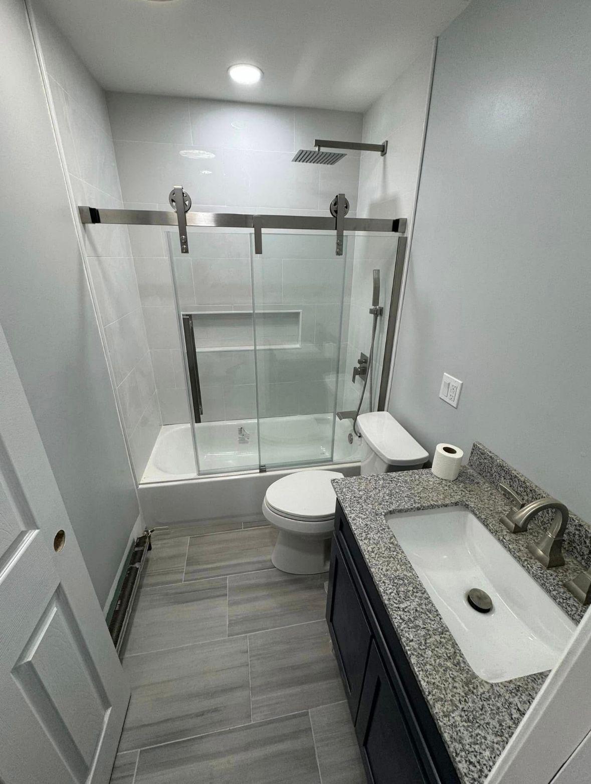Compact gray bathroom with walk-in glass shower, toilet, and granite vanity.