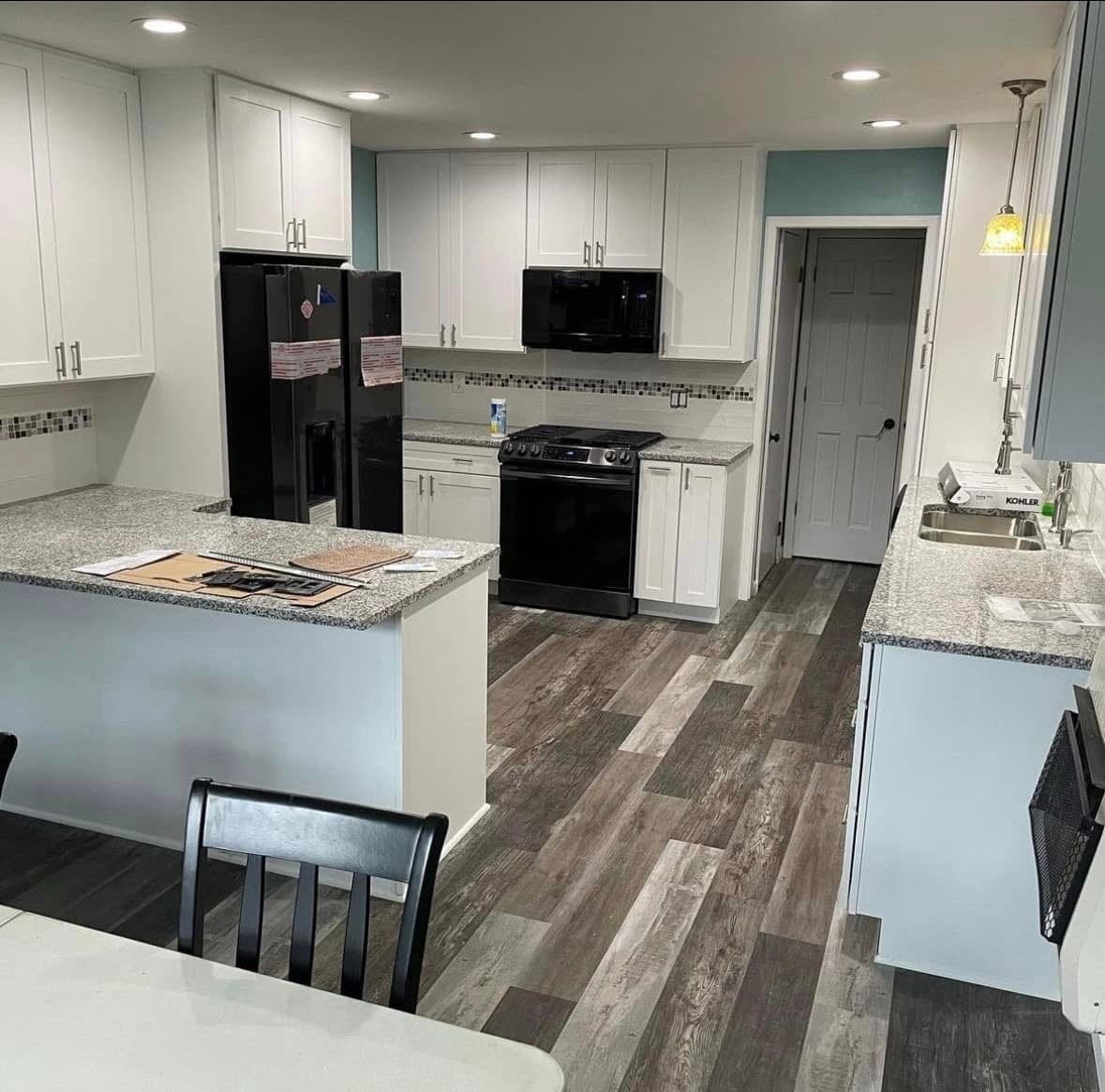 Modern white kitchen with black appliances, gray flooring, and granite countertops