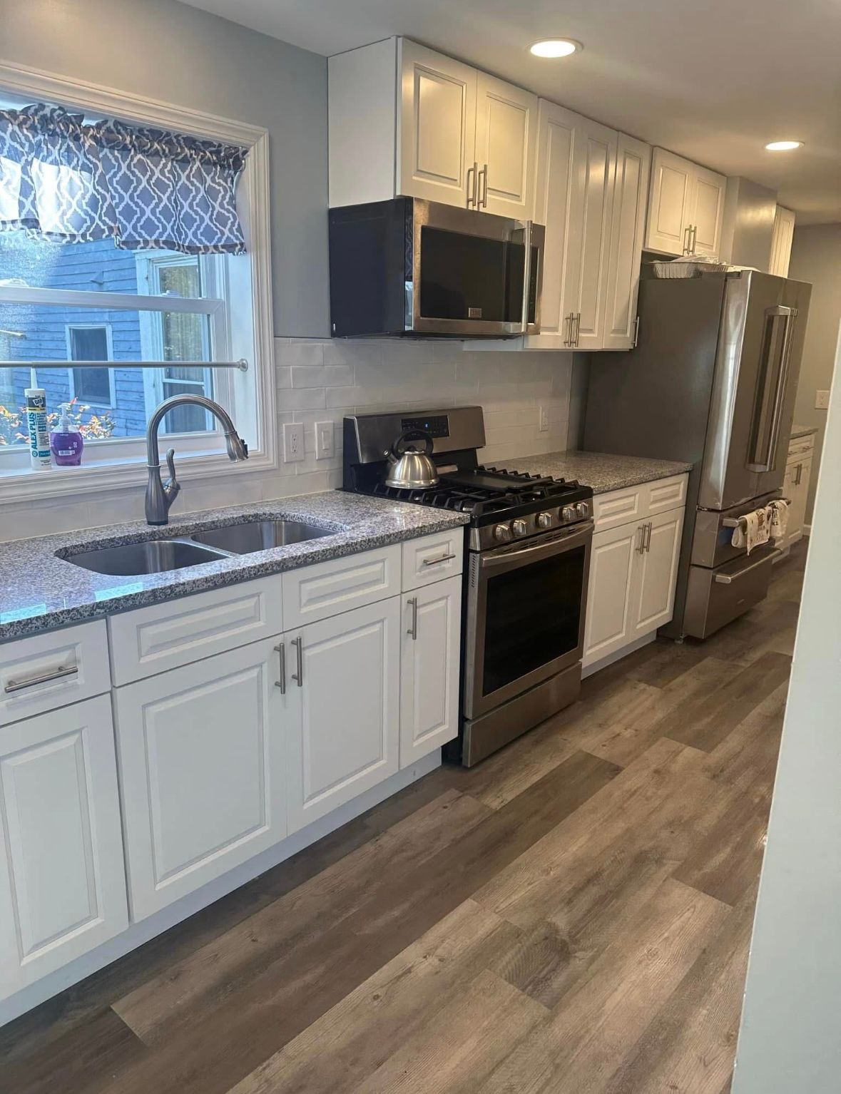 Bright modern kitchen with white cabinets, stainless appliances, gray countertops, and wood-look flooring