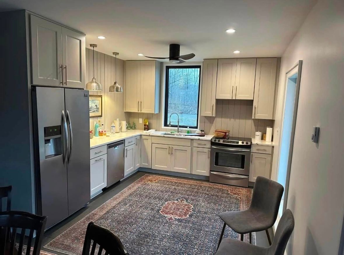 Modern kitchen with light cabinets, stainless appliances, window over sink, patterned rug, and chair by the door