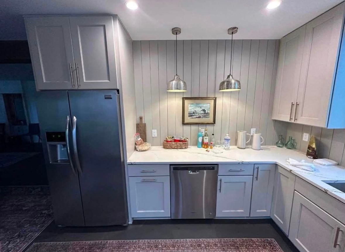 Modern kitchen with gray cabinets, stainless fridge, pendant lights, and white countertops