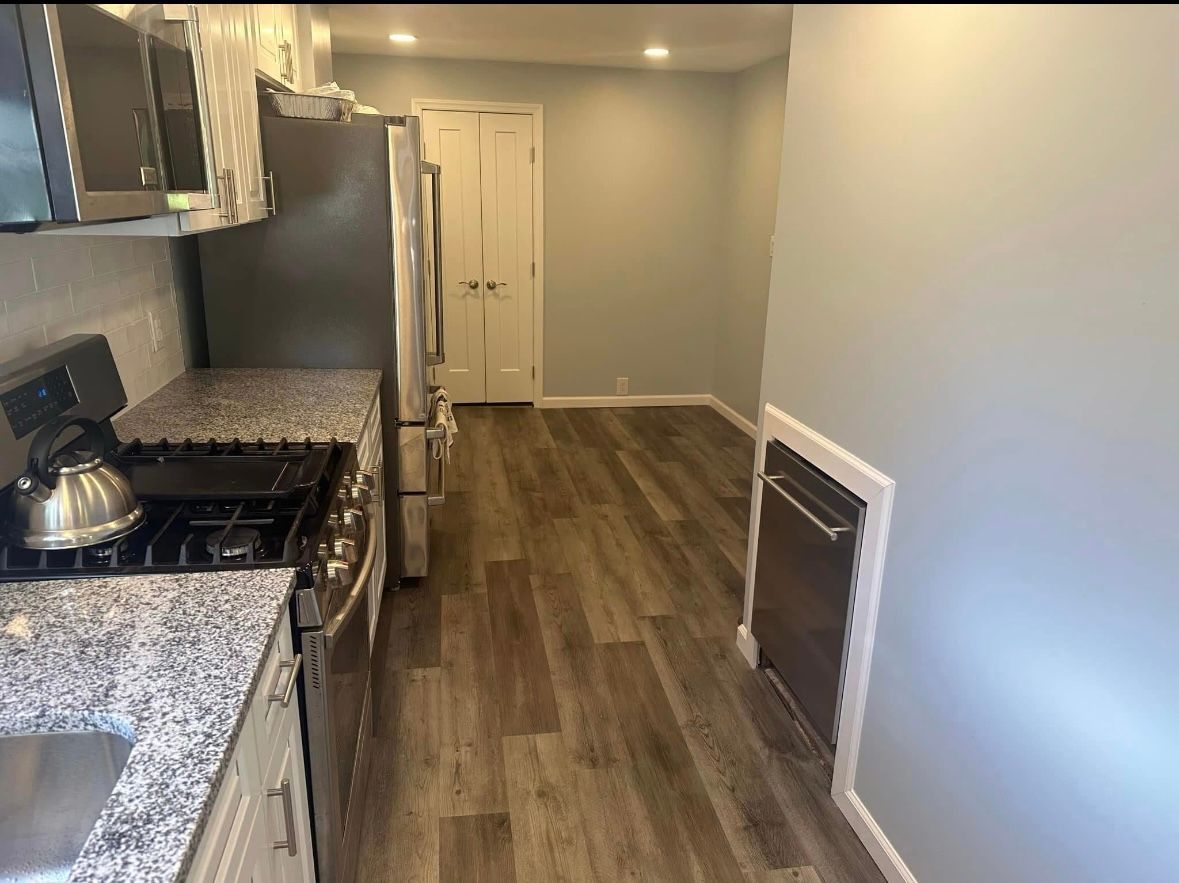 Narrow kitchen with stainless steel appliances, gray cabinets, granite countertop, and wood-look flooring.