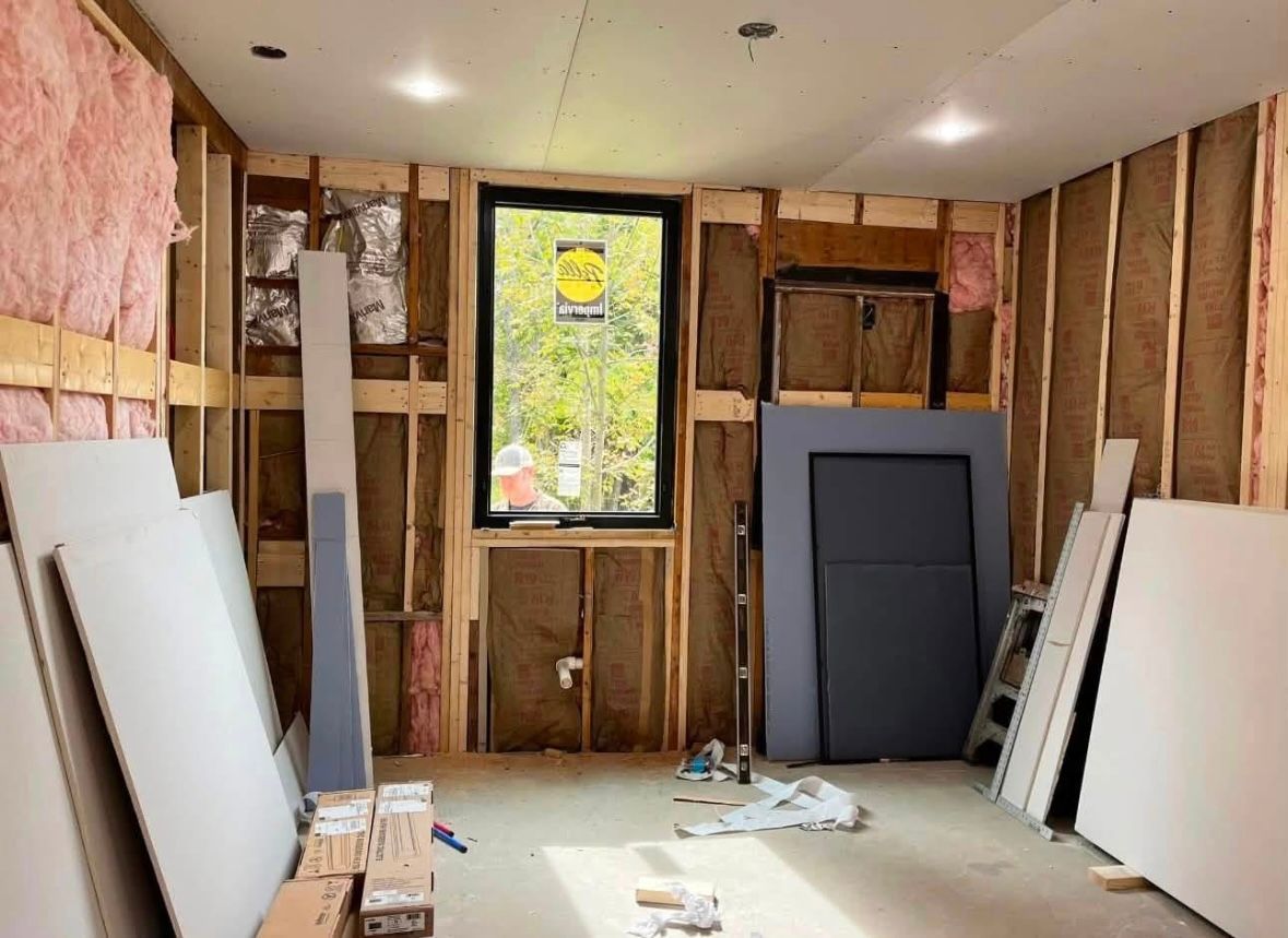 Unfinished room with exposed insulation, drywall panels, and a window at the far end