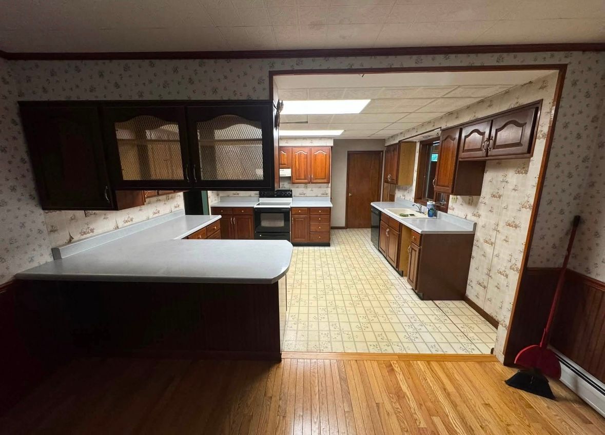 Spacious kitchen with wood floors, white counters, dark cabinets, and tiled flooring in the back.