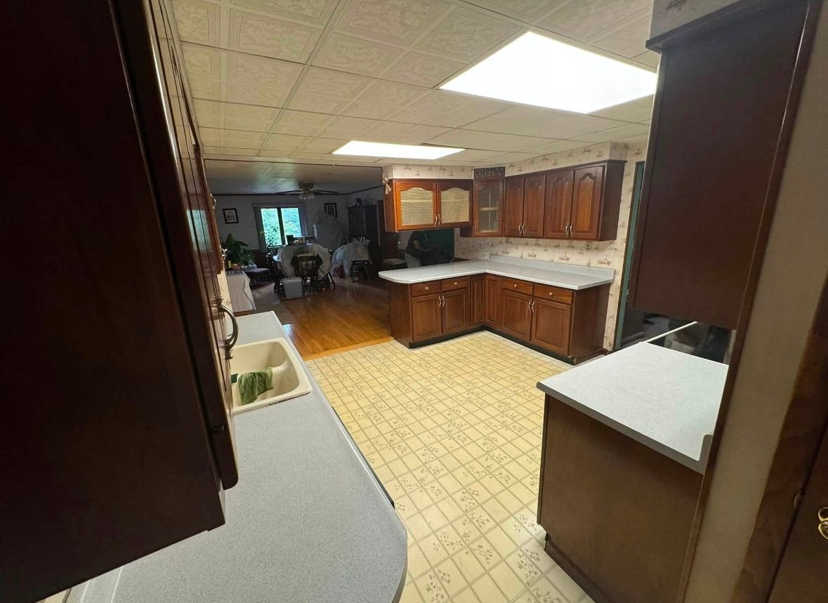 Kitchen with wood cabinets, white countertops, and yellow tile flooring, viewed from a doorway.