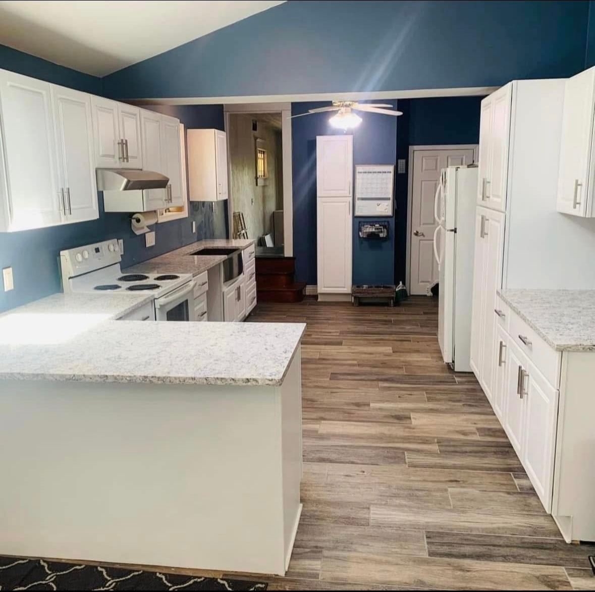 Bright kitchen with white cabinets, blue walls, and wood-look flooring, viewed from the island.