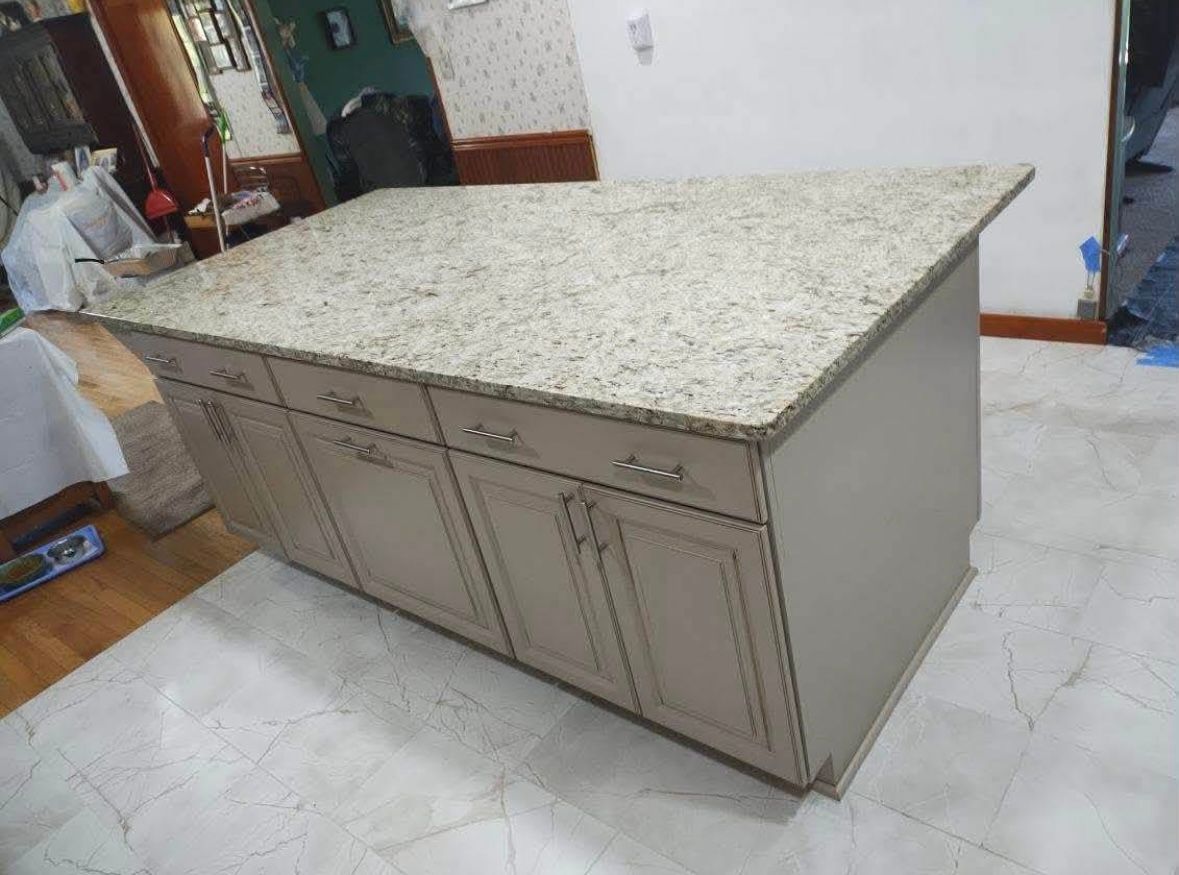 Large kitchen island with speckled granite countertop and light gray cabinet base in a tiled kitchen.