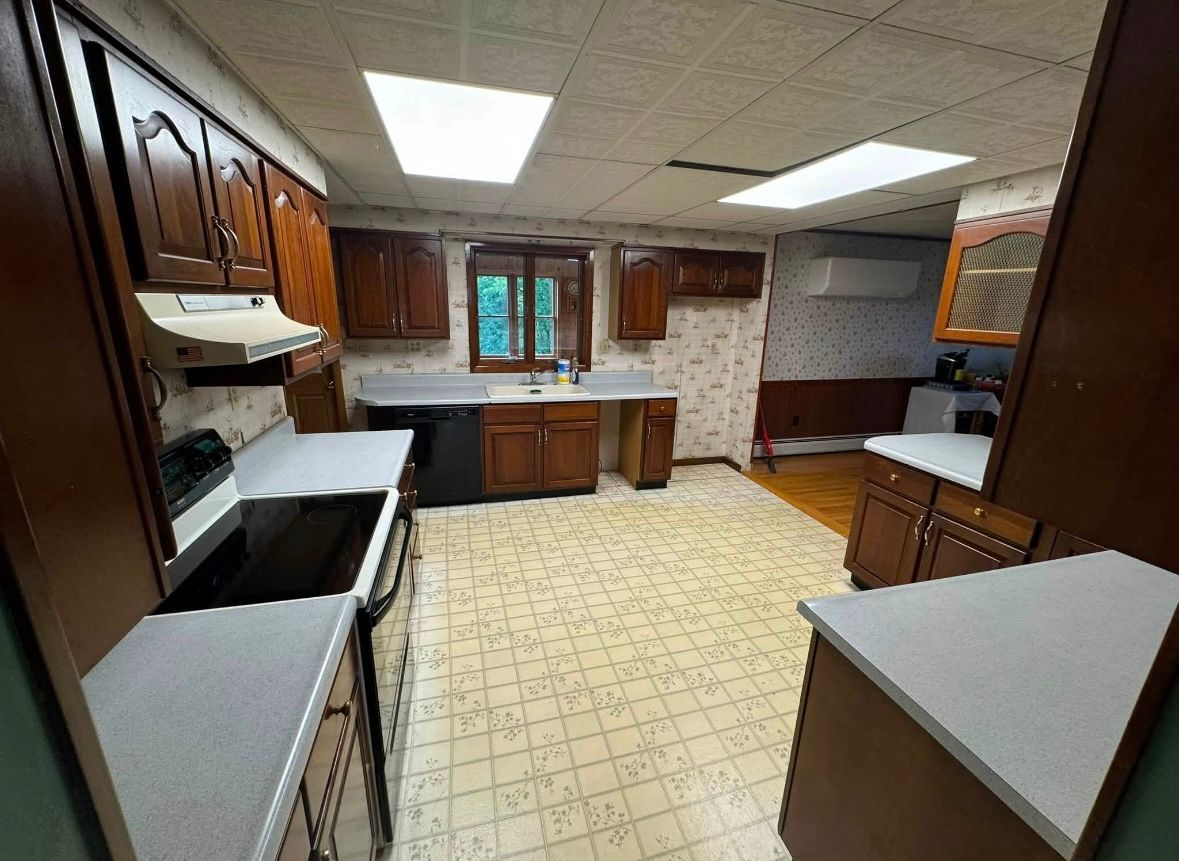 Empty kitchen with wooden cabinets, white countertops, tiled floor, and a window over the sink.