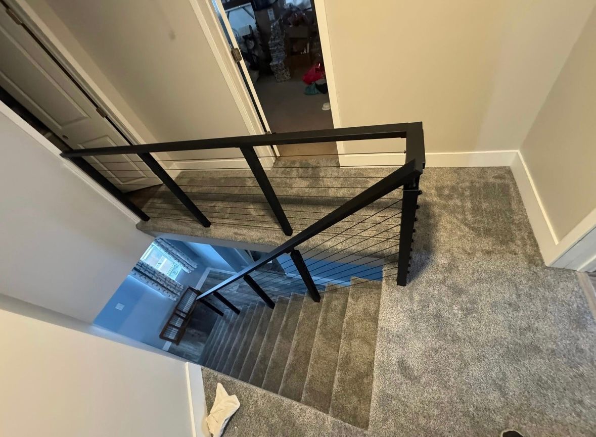 Indoor staircase with black metal railing and gray carpet, viewed from the top landing.