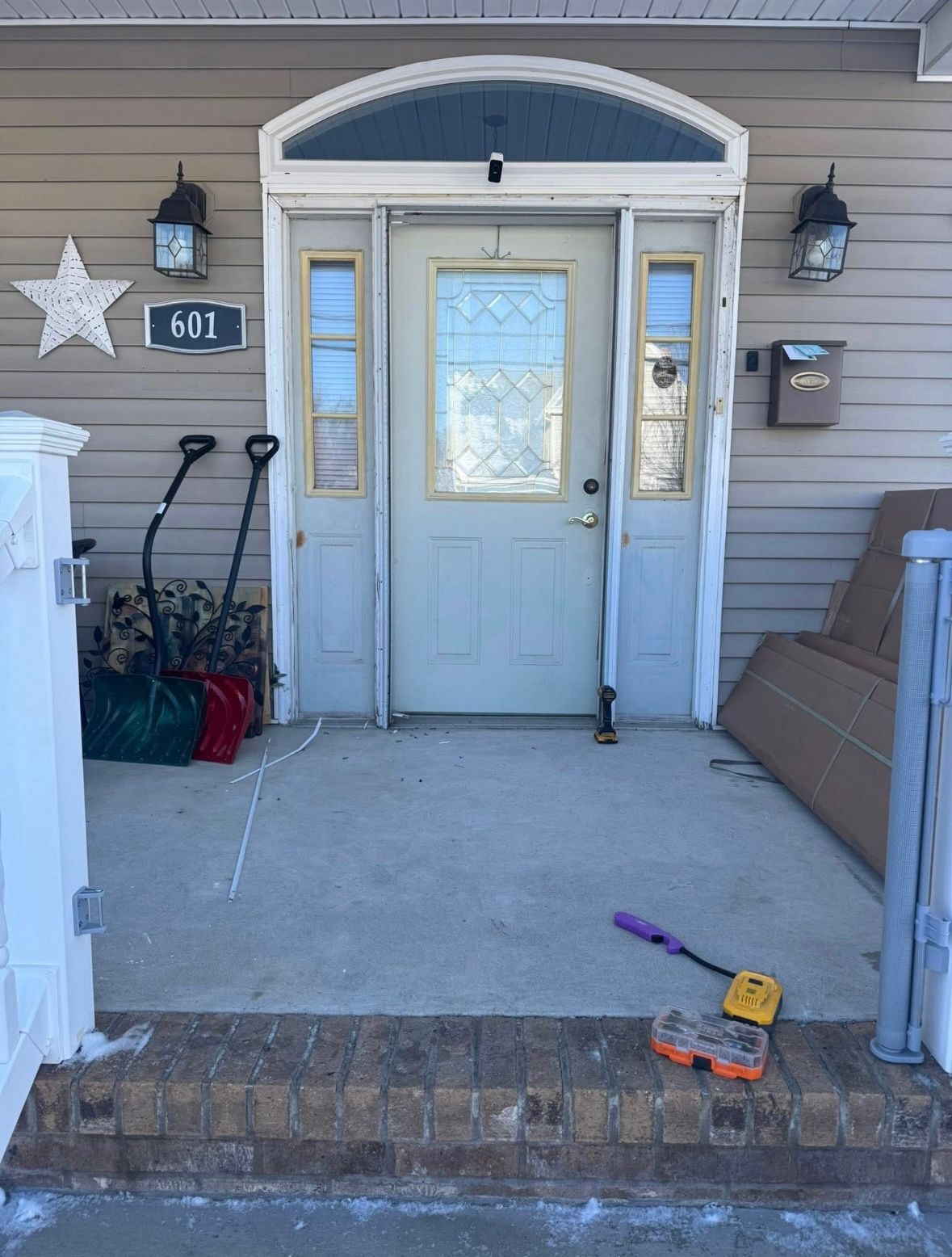 Front porch with a light blue front door, steps, doormat, and scattered items on the ground.